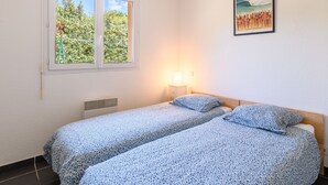 Un dormitorio con dos camas individuales, una ventana con vistas a zonas verdes, un cuadro en la pared y una mesita de noche con una lámpara.