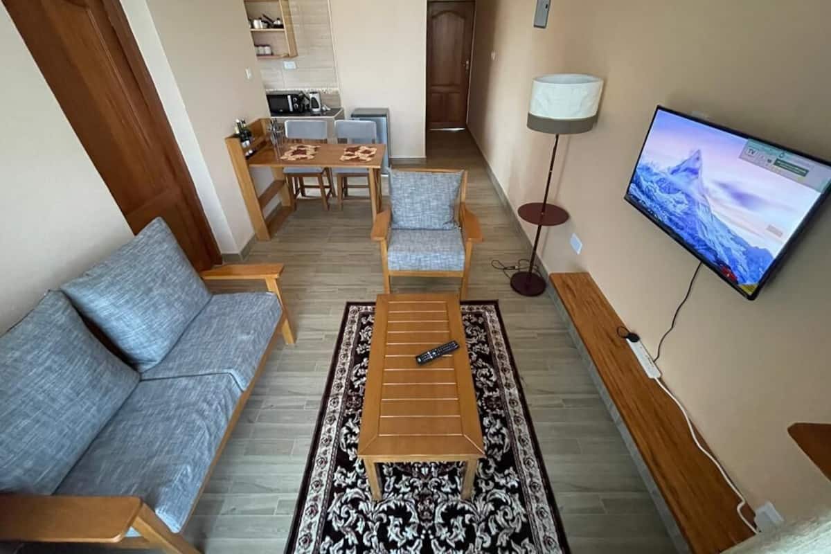 A living room with a sofa, a coffee table, a TV, and a kitchen in the background.