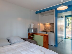 Una habitación pequeña con cama, kitchenette y vista al exterior.