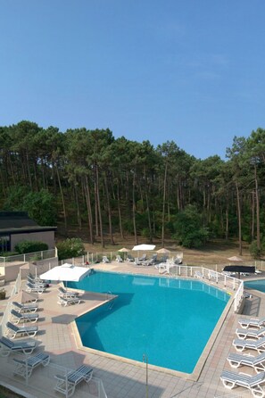 A rectangular swimming pool with a tiled deck, surrounded by lounge chairs and umbrellas.