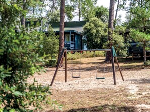 A playground with swings and a sandbox in a wooded area.
