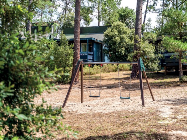 A playground with swings and a sandbox in a wooded area.