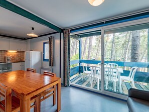 Una cocina moderna con una mesa y sillas de madera, un refrigerador y una ventana con vistas a un balcón con sillas de plástico blanco.