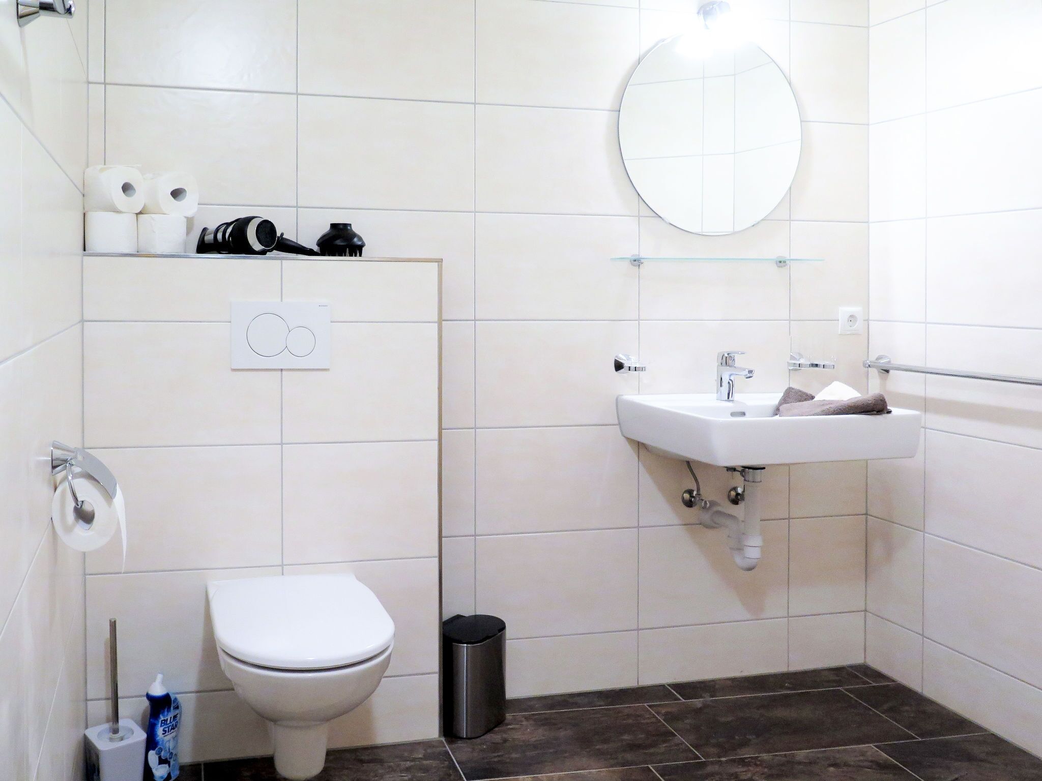 A bathroom with a toilet, a sink, a mirror, and a trash bin.