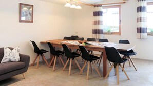 Un área de comedor con una mesa de madera y sillas negras, un sofá con un cojín estampado y un cuadro en la pared.