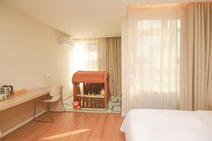 Une chambre d’hôtel comprenant un lit, un bureau avec une chaise, un petit espace de jeux et une fenêtre avec des rideaux.