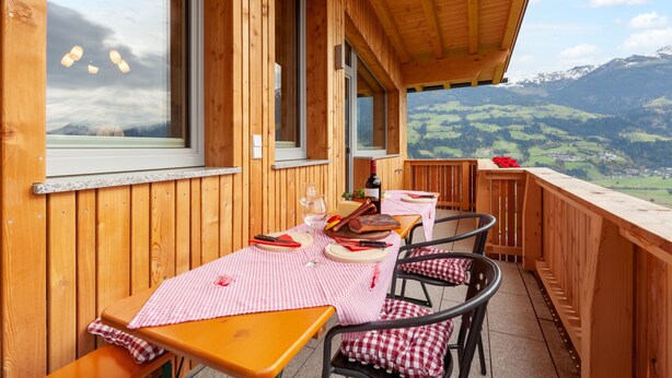 En träveranda med ett bord och stolar, med utsikt över ett bergigt landskap.