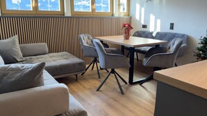 Una sala moderna con un sofá, sillas, una mesa de comedor y vistas a montañas nevadas a través de amplios ventanales.