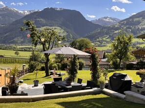 Eine Terrassenanlage im Freien mit Tisch und Stühlen, umgeben von Topfpflanzen und einem großen Sonnenschirm.