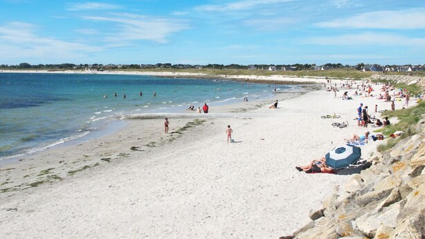 A beach with people sunbathing and swimming.