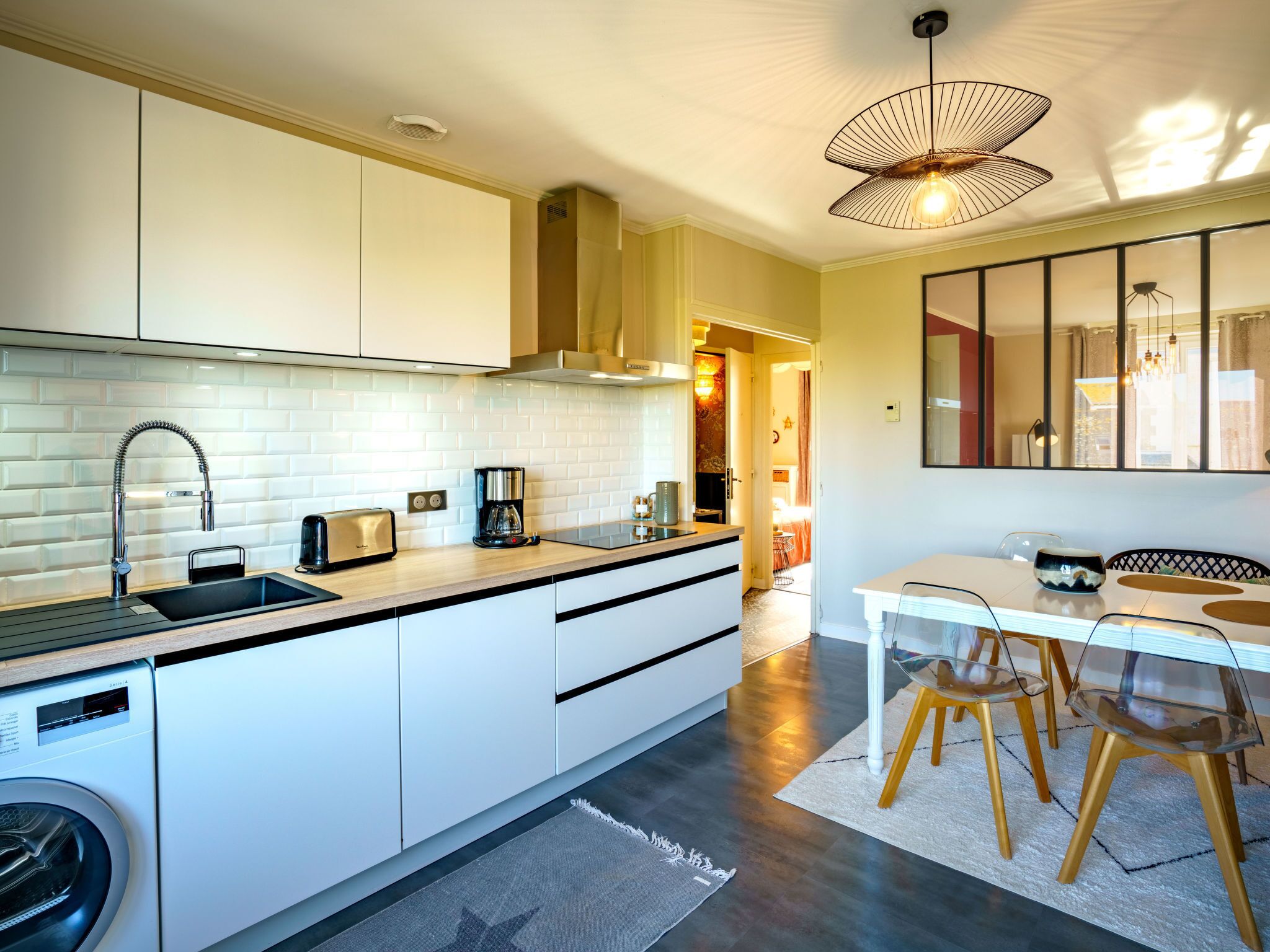 A modern kitchen with a built-in washing machine, a coffee maker, and a dining area with a table and chairs.