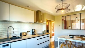 A modern kitchen with a built-in washing machine, a coffee maker, and a dining area with a table and chairs.