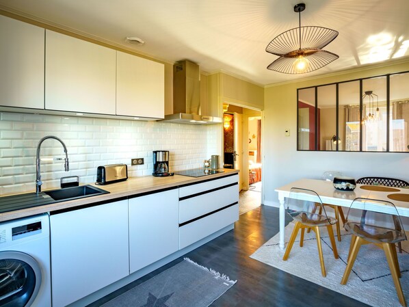 A modern kitchen with a built-in washing machine, a coffee maker, and a dining area with a table and chairs.