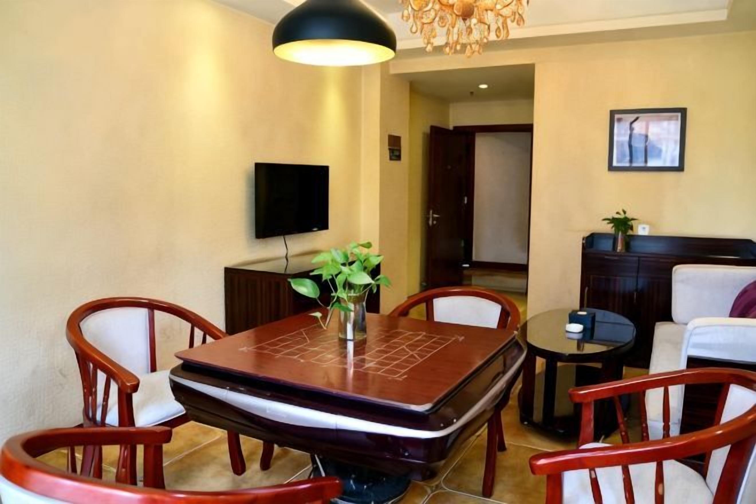 A dining area with a rectangular table, four chairs, a small round table, and a television mounted on the wall.