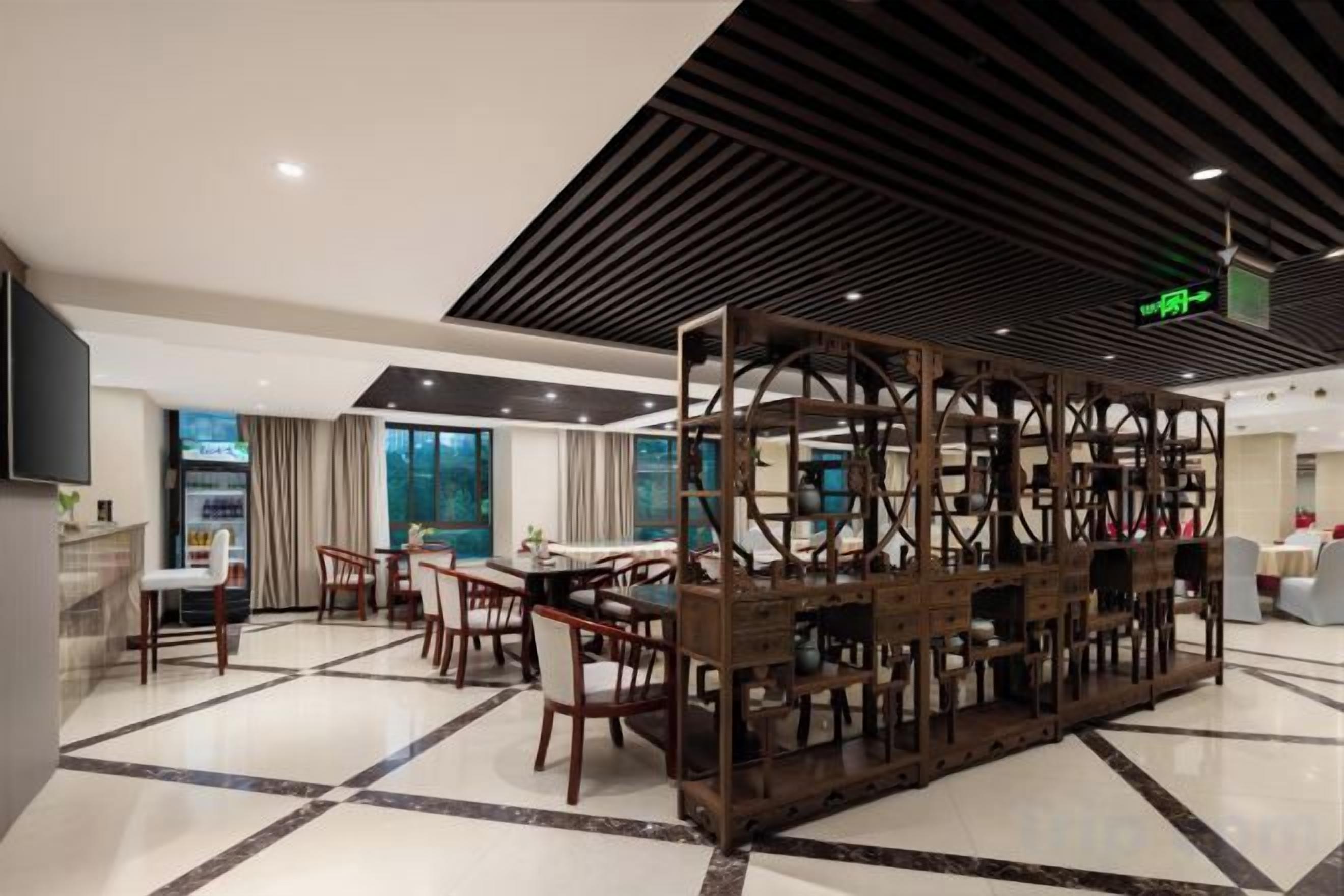 A modern dining area with a central wooden structure, multiple tables and chairs, and a flat-screen TV mounted on the wall.
