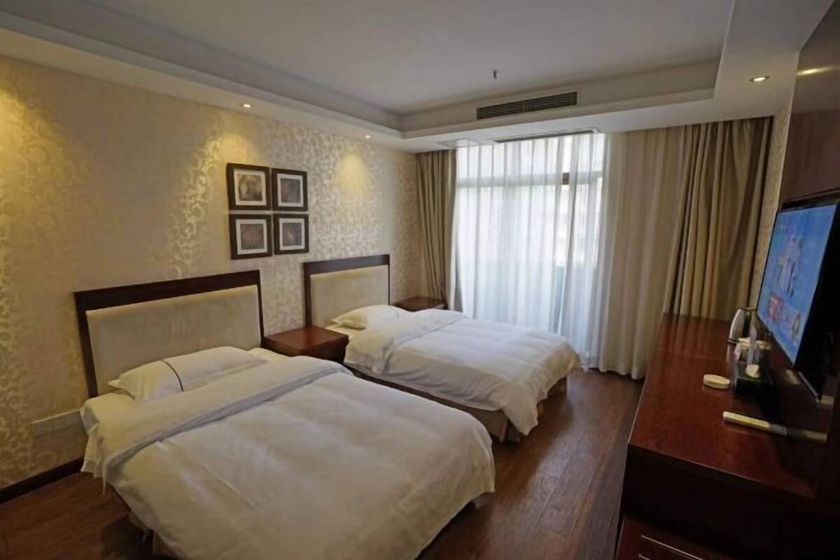 A hotel room with two beds, a TV, and a large window with curtains.