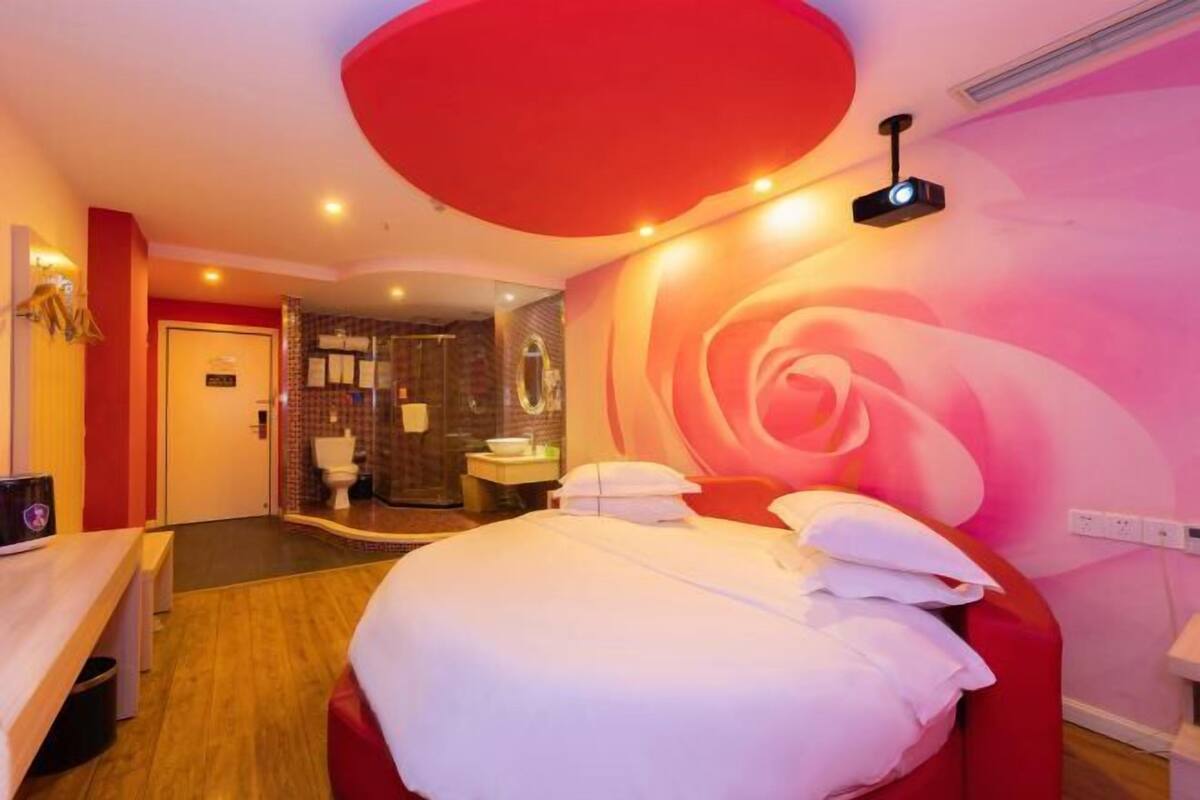 A hotel room with a large bed, a bathroom with a shower, and a red accent wall.