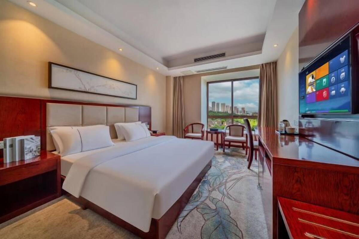 A hotel room with a bed, a desk, a television, and a window with a city view.