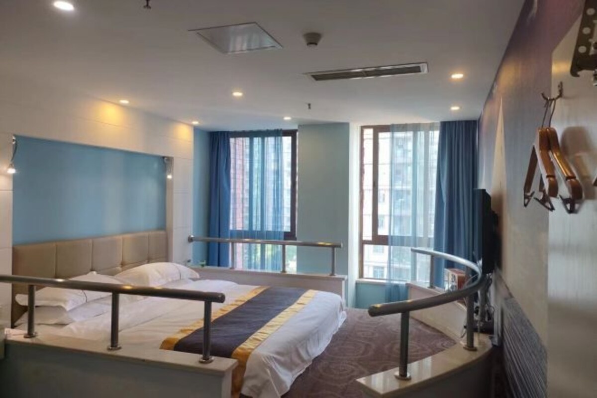 A hotel room with two beds, a window with curtains, a wall-mounted heater, and a railing.
