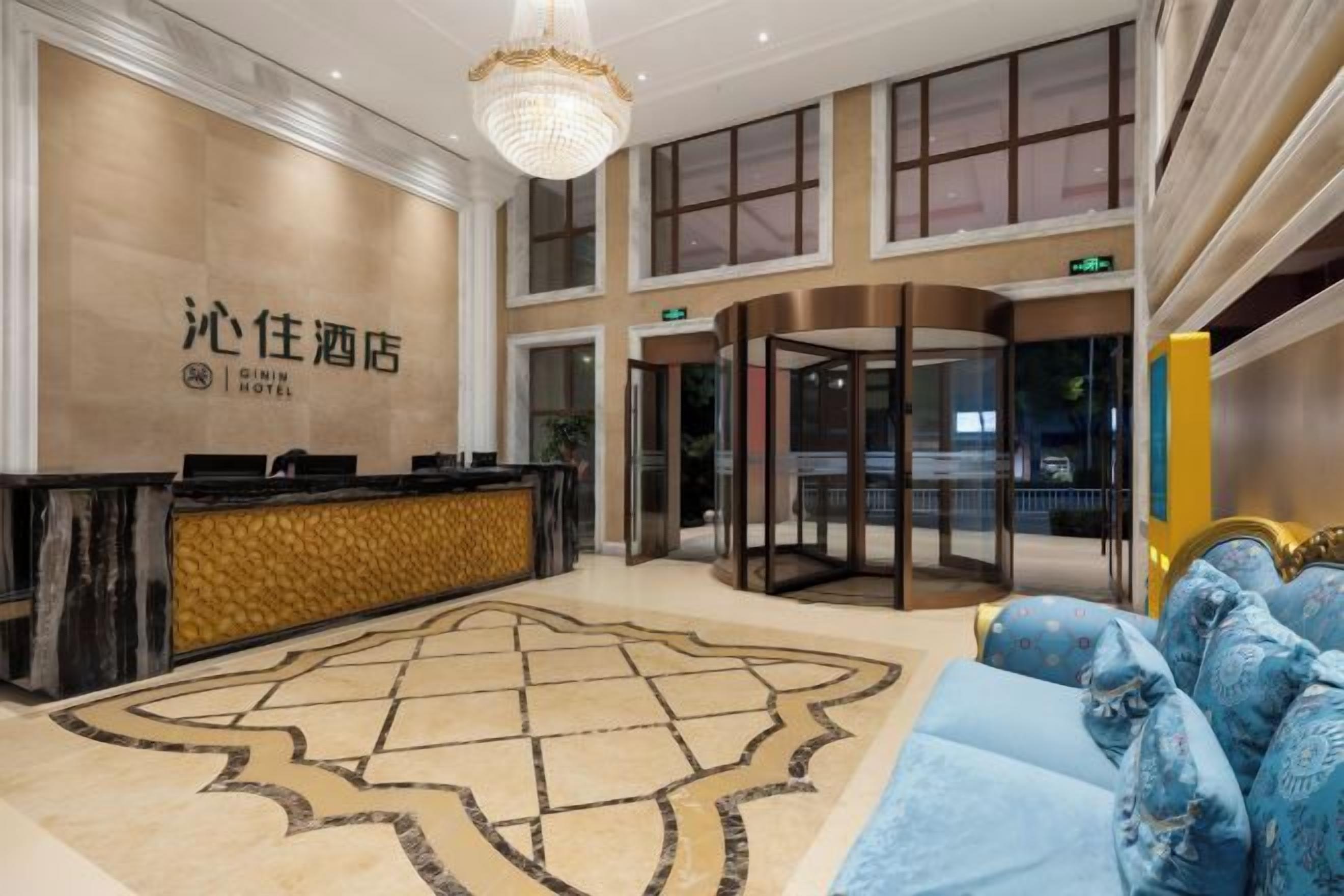 Un vestíbulo de hotel con mostrador de recepción, alfombra estampada, sofá azul y puerta giratoria.