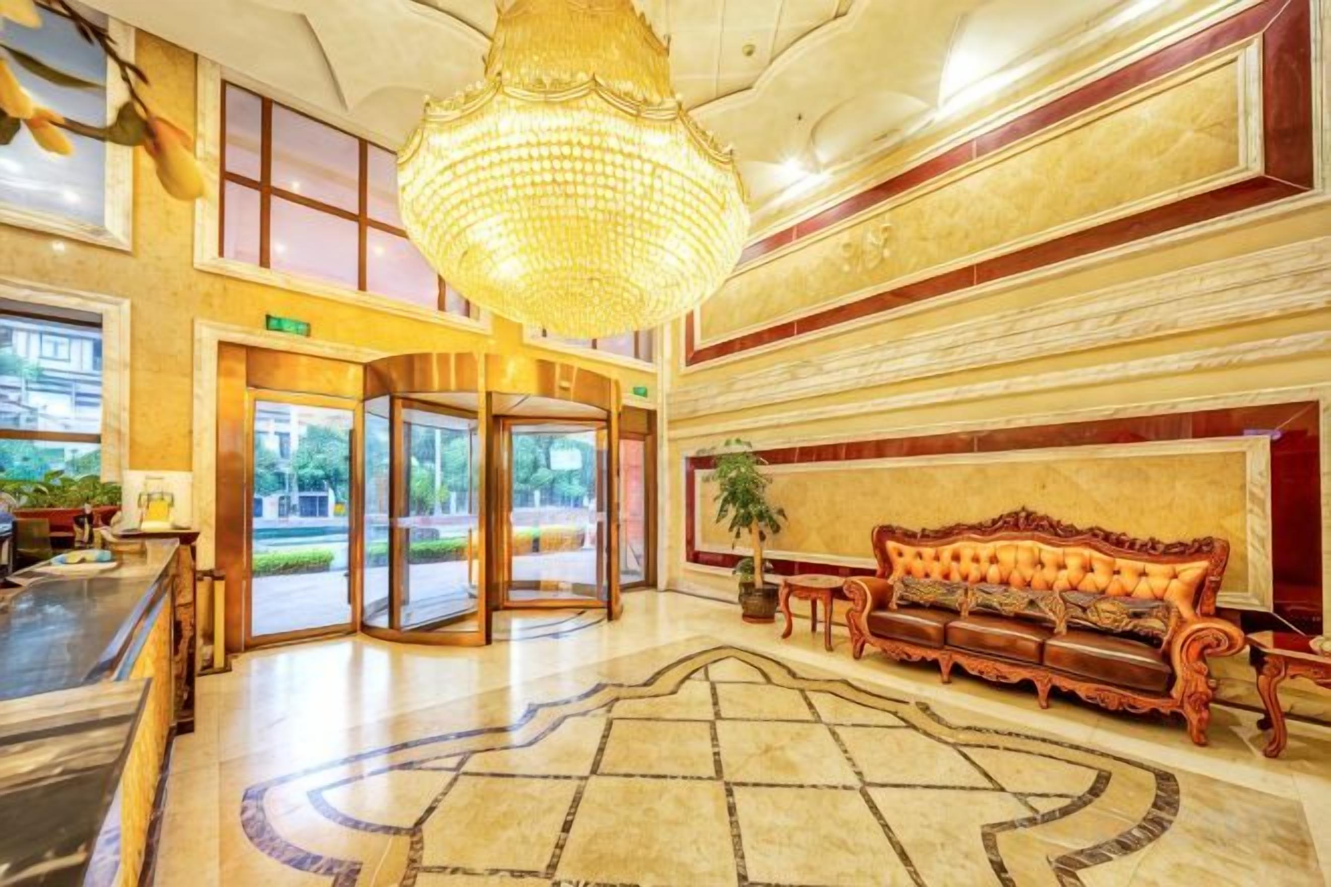 A lobby with a grand chandelier, a revolving door, and a plush sofa.
