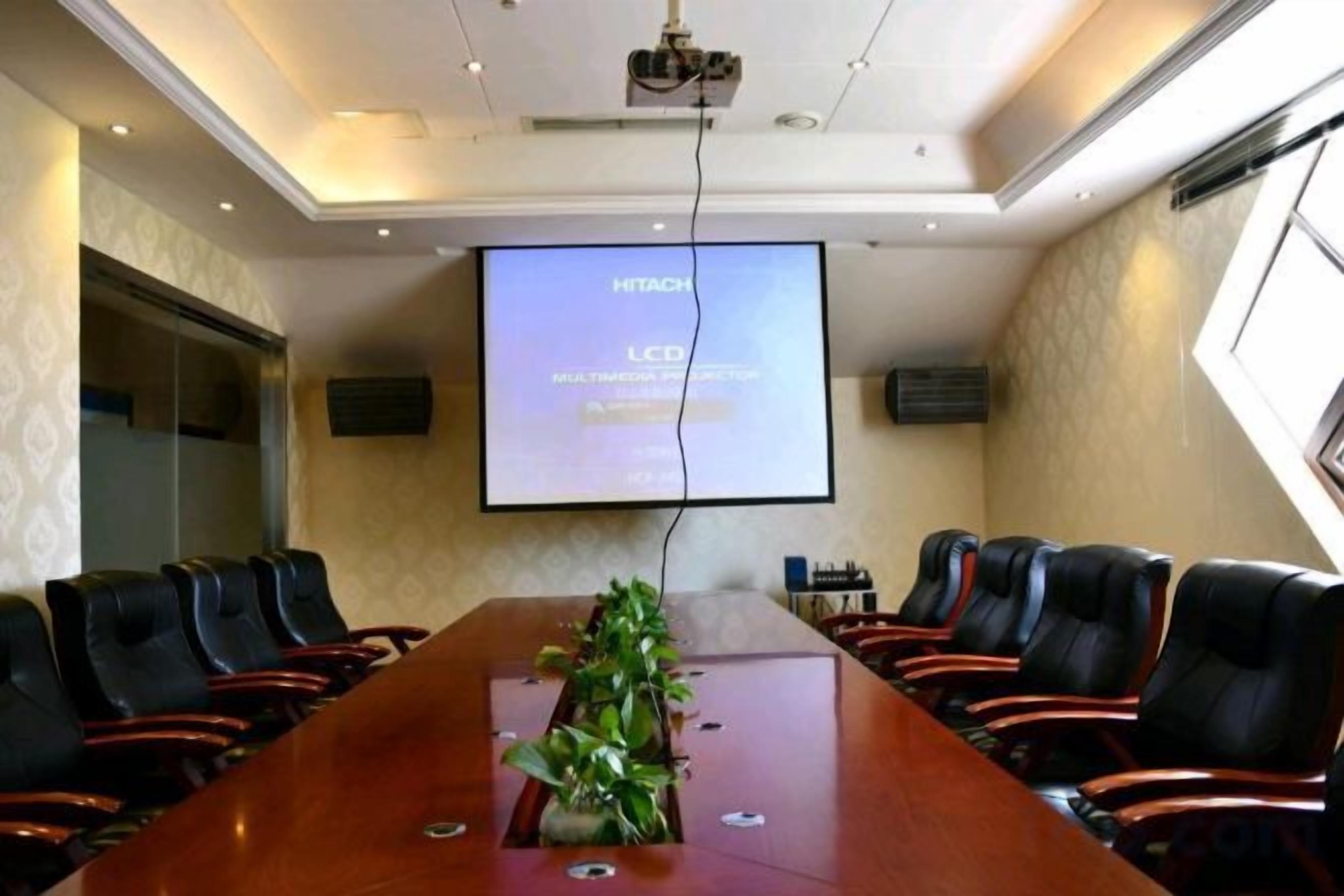 A conference room with a long table, multiple chairs, a projector screen, and a plant on the table.