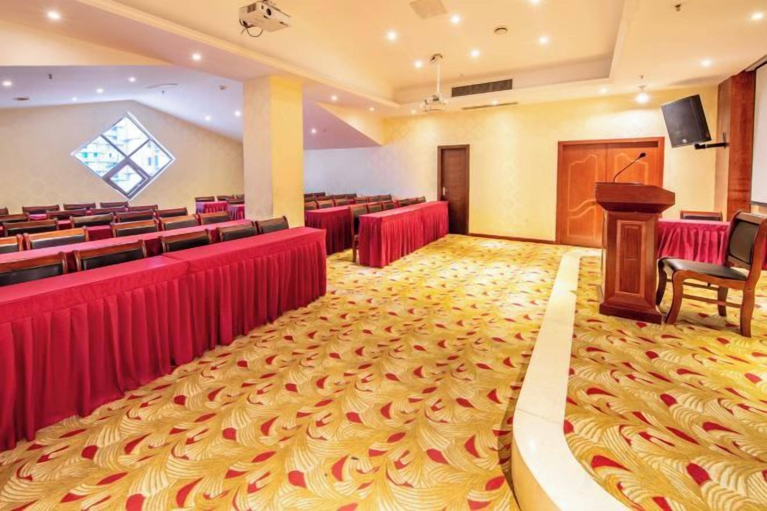 A conference room with rows of tables, a podium, and a large window.