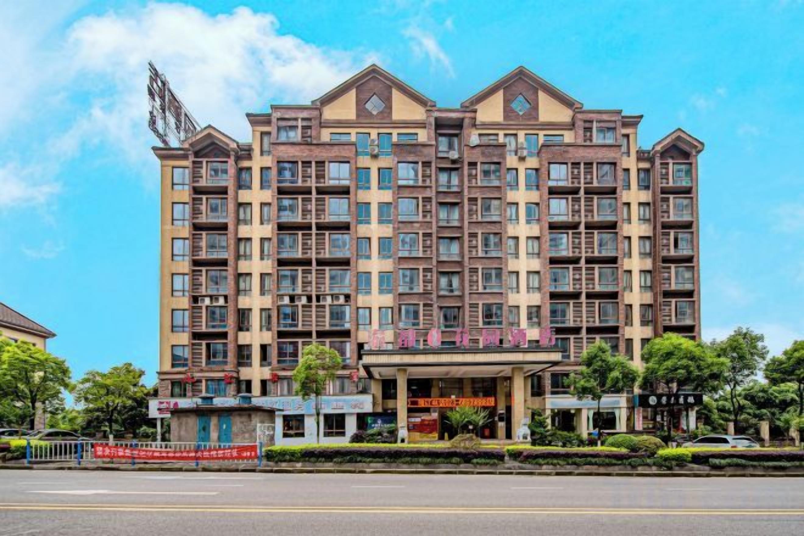 A multi-story hotel with a central entrance, balconies, and a clear sky.
