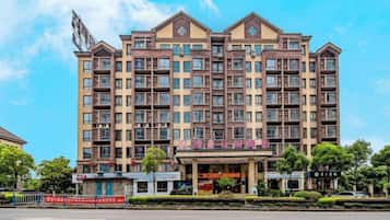 A multi-story hotel with a central entrance, balconies, and a clear sky.