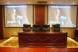 Une salle de conférence équipée d’un bureau en bois, de quatre fauteuils en cuir et de deux grands écrans de projection affichant du texte.
