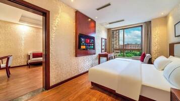 A hotel room with a large bed, a TV mounted on the wall, and a view of buildings through the window.