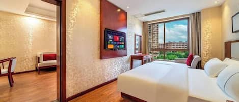 A hotel room with a large bed, a TV mounted on the wall, and a view of buildings through the window.