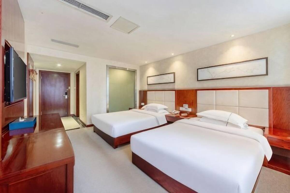 A hotel room with two beds, a desk, a television, and a door leading to another room.