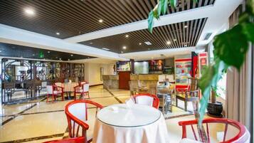 Un hall de hotel con zona de bar, diferentes disposiciones de asientos y una planta grande.