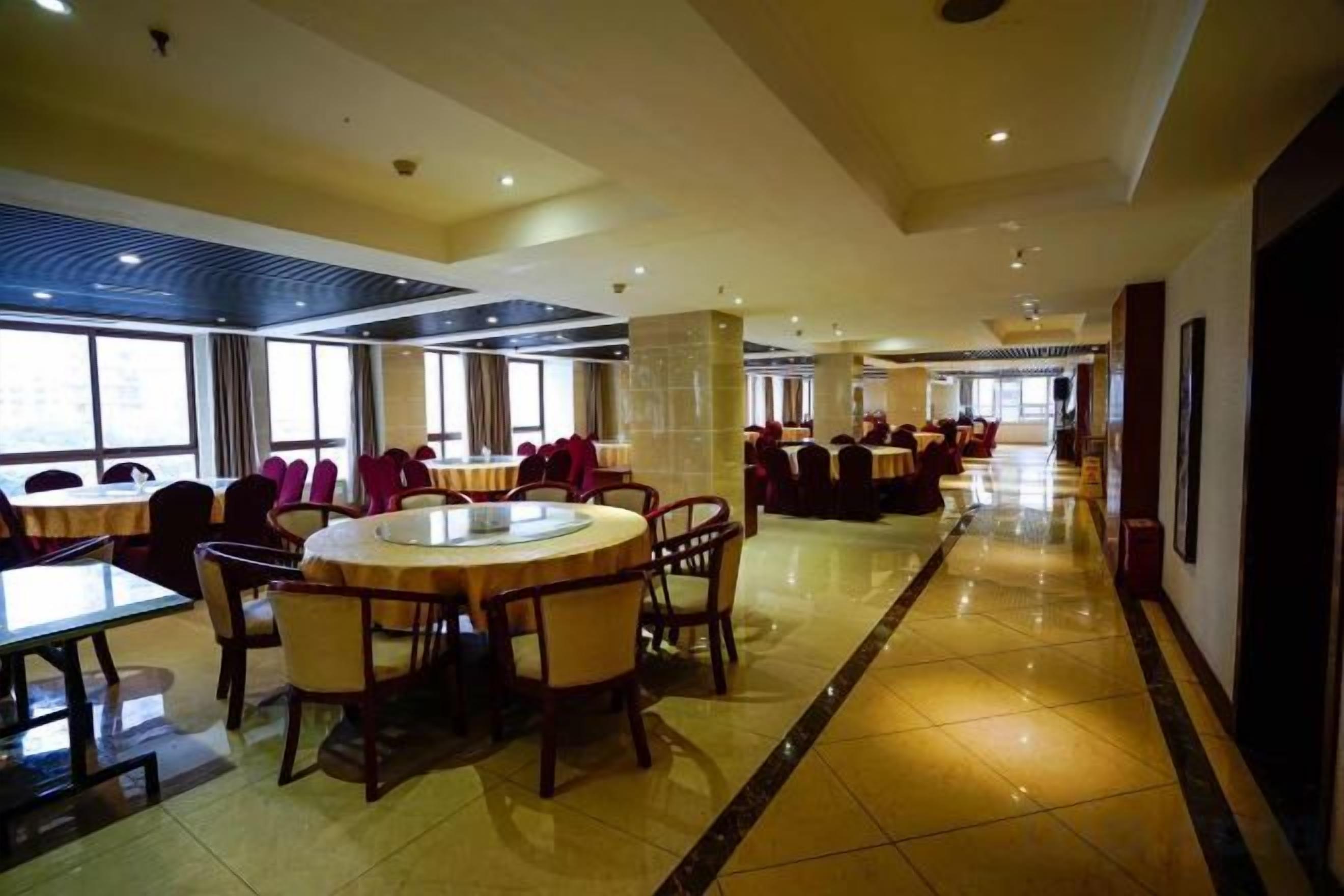 A spacious hotel lobby with a central round table, multiple seating areas, and large windows providing natural light.