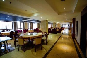 Un hall d’hôtel spacieux, doté d’une grande table ronde au centre, de plusieurs espaces de détente et de larges fenêtres laissant entrer la lumière naturelle.