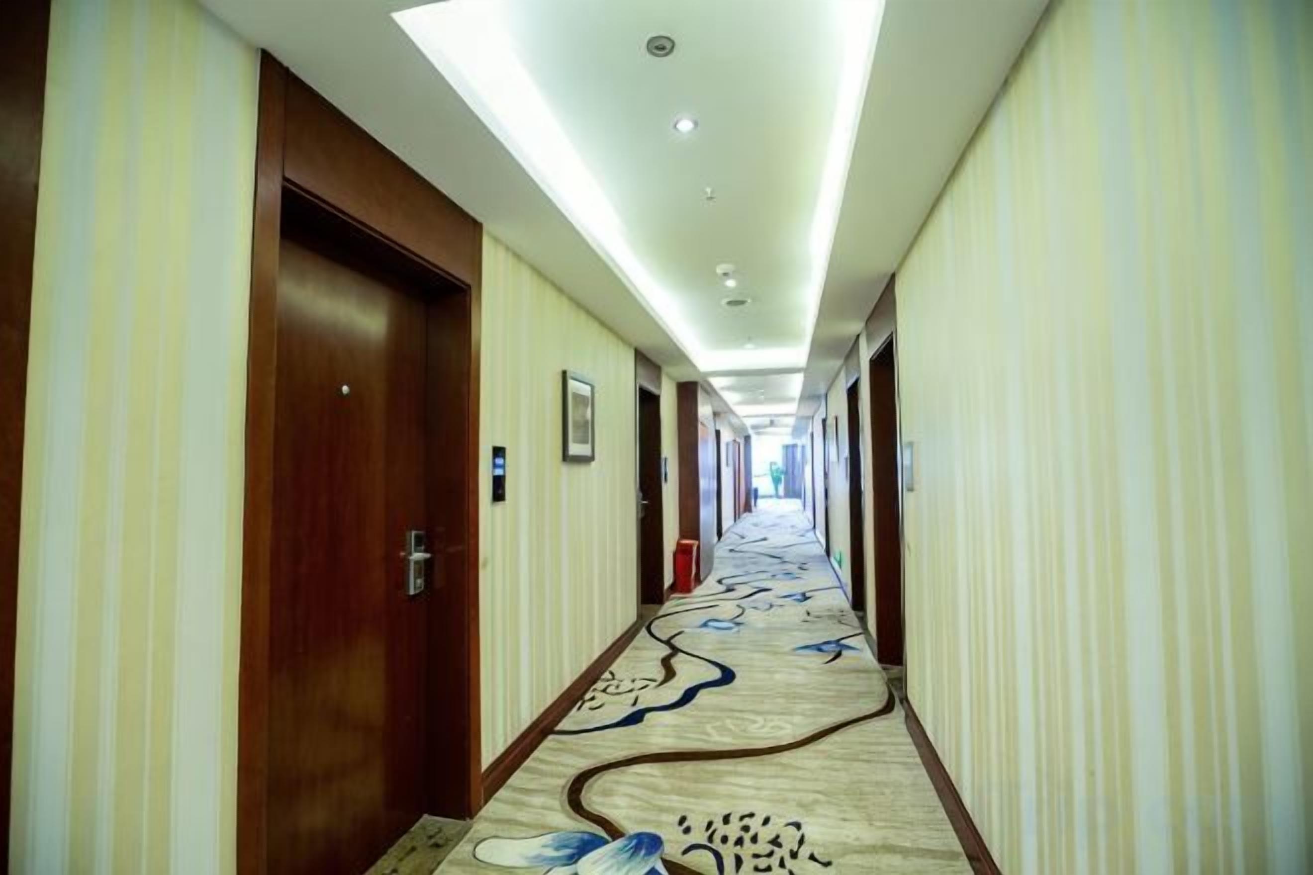 Pasillo de hotel con puertas a ambos lados, una alfombra estampada y una lámpara en el techo.