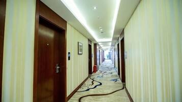 Pasillo de hotel con puertas a ambos lados, una alfombra estampada y una lámpara en el techo.
