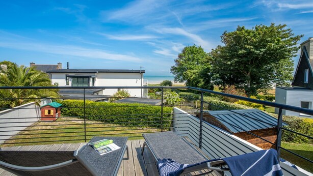 Un balcon avec mobilier d’extérieur, une petite maison de jeu et une vue sur une maison moderne et la plage.
