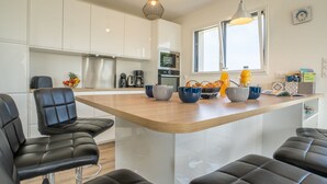 Une cuisine moderne avec des armoires blanches, un plan de travail en bois et des chaises en cuir noir. On y trouve deux lampes suspendues, un four à micro-ondes et une machine à café sur le plan de travail.