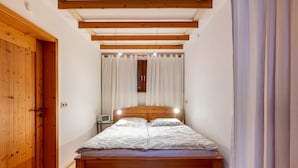 Ein Schlafzimmer mit einem hölzernen Bett, weißen Vorhängen, einem Nachttisch und einem Holzschrank.