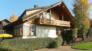 A two-story wooden house with a balcony, a visible window, and a yellow umbrella. - Apartment 'Gästehaus Helga Scherer' with Private Terrace, Garden and Wi-Fi (Ballrechten-Dottingen)