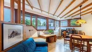 Ein modernes Interieur mit Holzbalkendecke, großen Fenstern, einer Essecke und einem Sofa.
