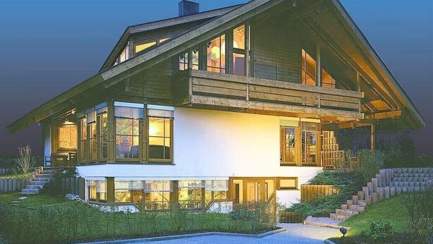 Ein modernes, zweistöckiges Haus mit großen Fenstern, einem geneigten Dach und einer gut beleuchteten Fassade.