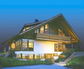 A modern two-story house with large windows, a sloped roof, and a well-lit exterior.
