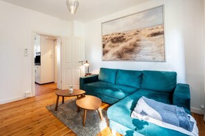 A living room with a teal sofa, a small wooden table, a rug, and a painting on the wall.