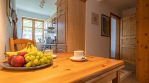 Une table de salle à manger en bois, avec un panier de fruits, une tasse et une assiette.