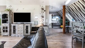 Un salon moderne avec un canapé en cuir, un téléviseur à écran plat et une cuisine en arrière-plan.