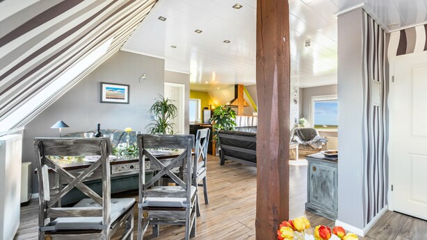 Un intérieur moderne comprenant un coin repas, des chaises en bois, un canapé et une vue sur l’extérieur.