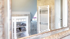 Une salle de bain avec un porte-serviettes blanc, une étagère où sont pliés soigneusement des serviettes et un miroir qui reflète la pièce.